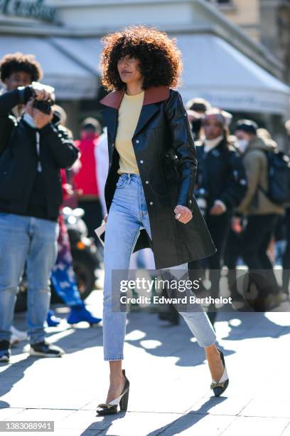 Guest wears a pale yellow pullover, blue faded denim skinny pants, a black shiny leather long coat, black and white shiny leather with gold nailed...