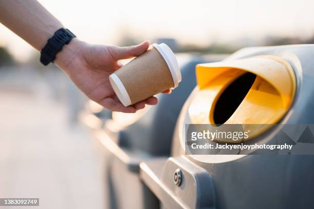 closeup hand throwing empty paper coffee cup in recycling bin. - recycling bin stock pictures, royalty-free photos & images