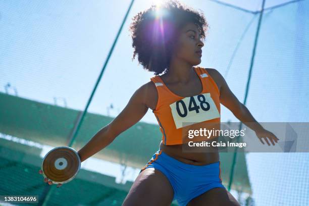 female track and field athlete throwing discus under sunny blue sky - bib stock pictures, royalty-free photos & images