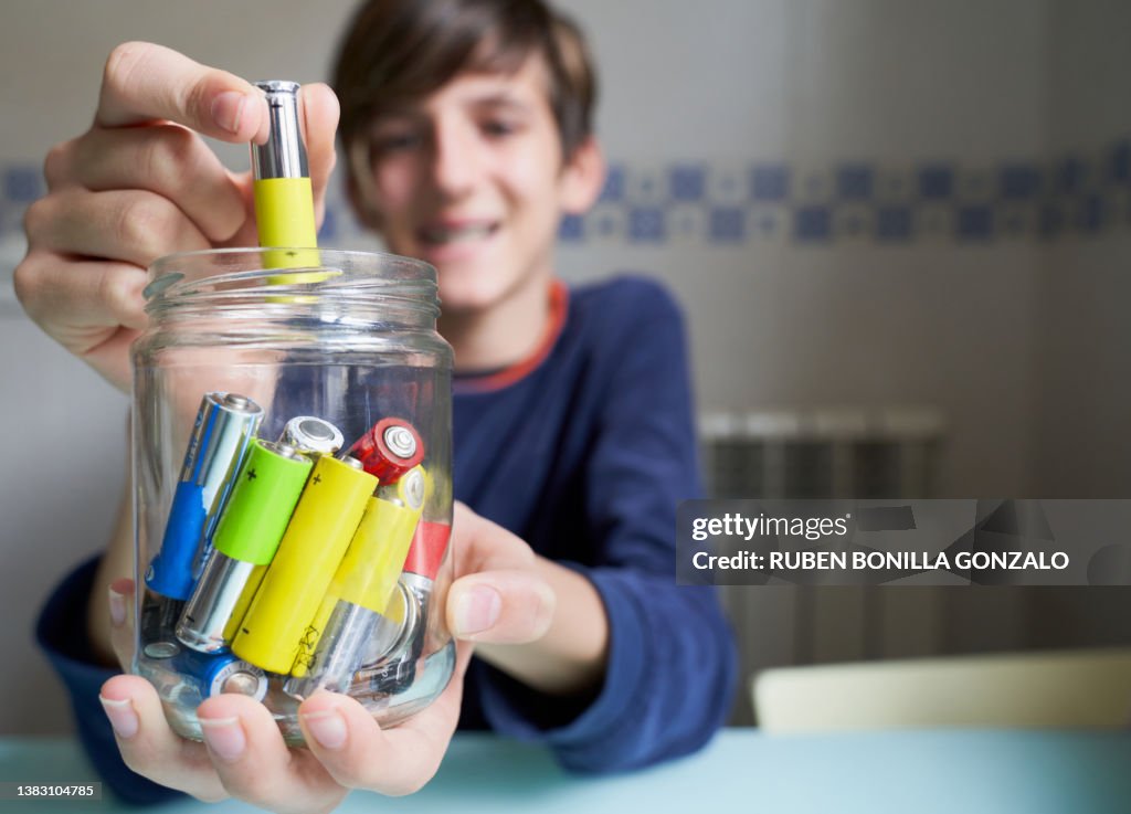 Caucasian teenager Putting Used Batteries Into Glass Jar For Recycling. Environmental concept.