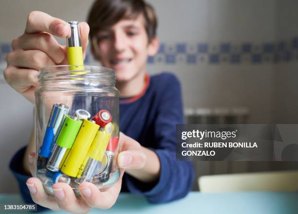 caucasian teenager putting used batteries into glass jar for recycling. environmental concept. - alkaline stock pictures, royalty-free photos & images