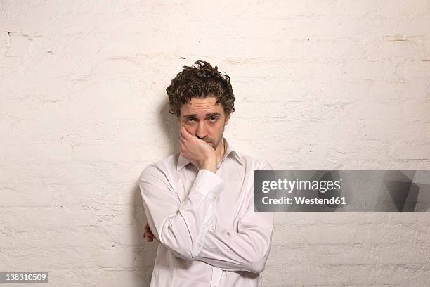 germany, hamburg, mid adult man leaning against wall, portrait - manos a la cabeza fotografías e imágenes de stock