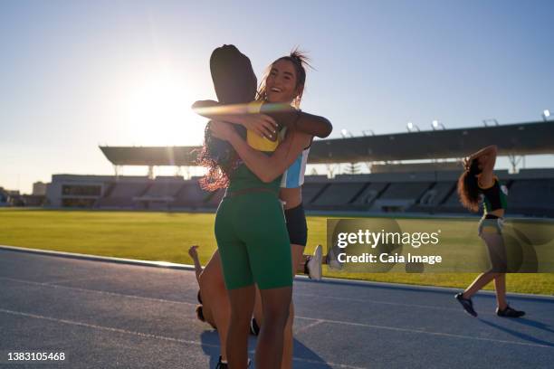 happy female track and field athletes hugging on sunny track - girls on train track stock pictures, royalty-free photos & images