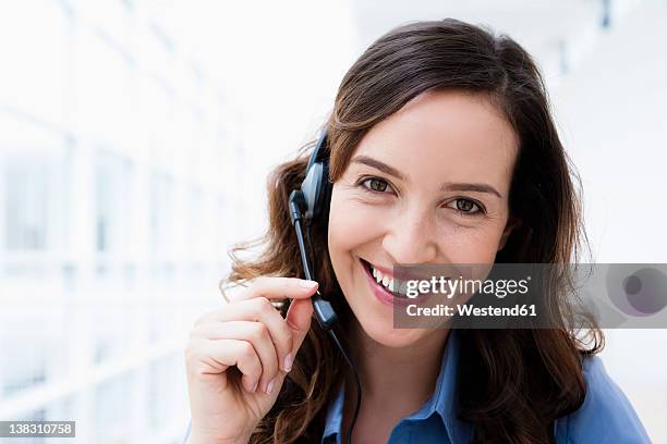 germany, bavaria, diessen am ammersee, young businesswoman using headset, smiling, portrait - call center stock-fotos und bilder