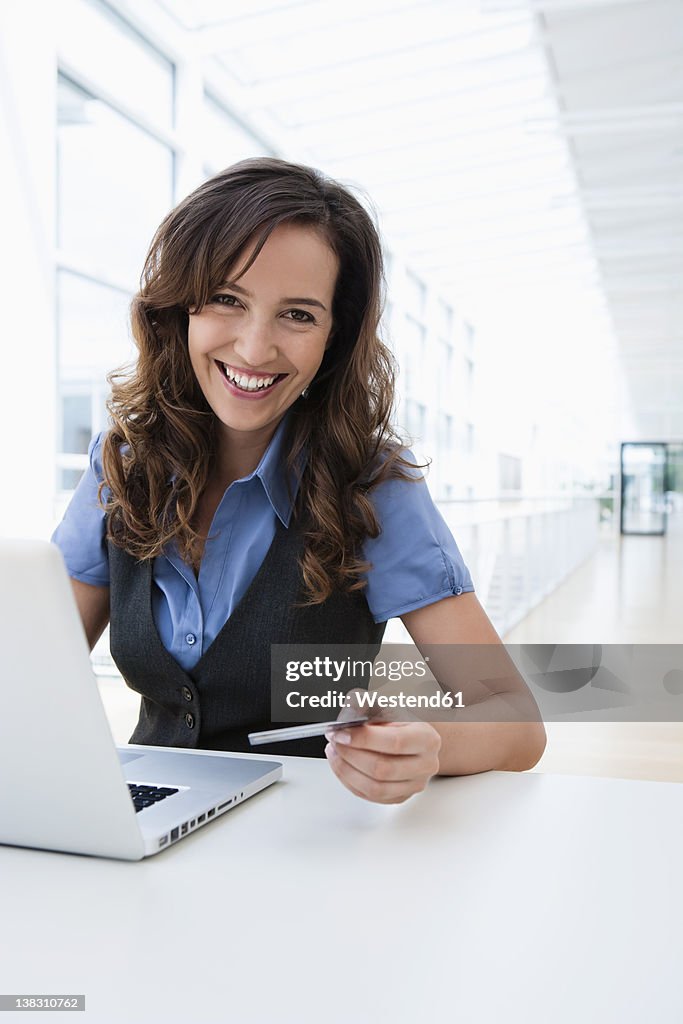 Germany, Bavaria, Diessen am Ammersee, Young businesswoman using laptop and holding credit card, smiling