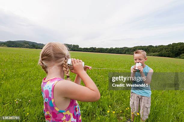 germany, north rhine-westphalia, hennef, boy and girl in meadow playing with tin can phone - tin can phone fotografías e imágenes de stock