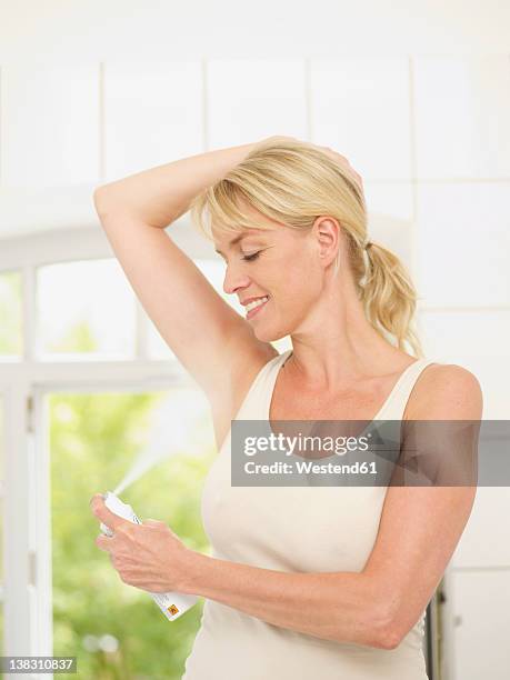 mature woman putting deodorant on underarms, smiling - deodorant stock-fotos und bilder