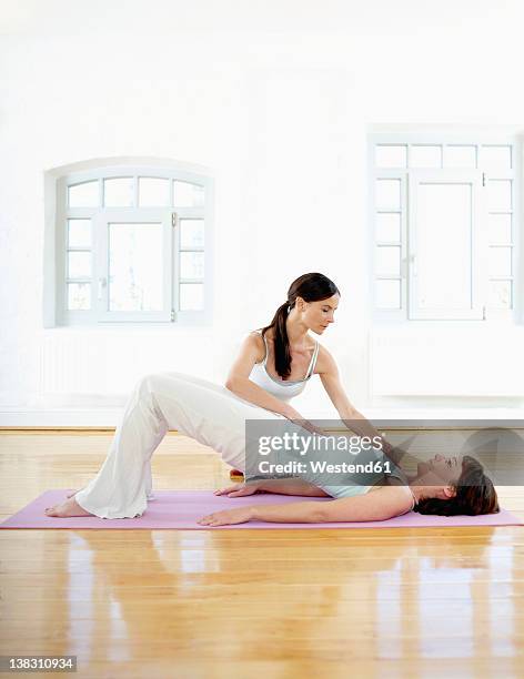 germany, hamburg, yoga instructor helping woman doing yoga exercise in gym room - pilates abstract stock pictures, royalty-free photos & images