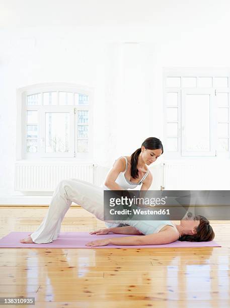 germany, hamburg, yoga instructor helping woman doing yoga exercise in gym room - pilates abstract stock pictures, royalty-free photos & images