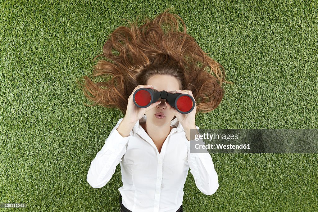 Young woman looking through binoculars while lying on grass