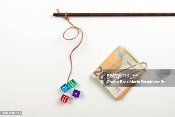 dangle two dices  on a stick and euro banknotes as gambling  addiction concept against light background - wooden stick stock pictures, royalty-free photos & images