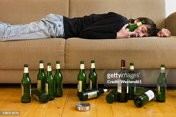 germany, hessen, frankfurt, drunk man lying on sofa with empty beer bottles - alcoholic stock-fotos und bilder