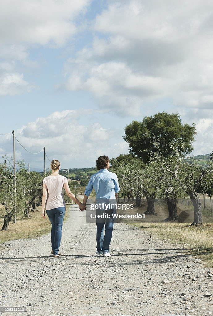 Italy, Tuscany, Young couple holding hands and walking on country road