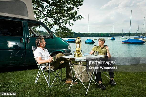 germany, bavaria, woerthsee, two men having drinks and talking near lakeshore while camping - only mid adult men stock pictures, royalty-free photos & images