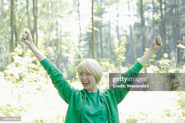 germany, bavaria, schaeftlarn, young woman in forest with arms up, portrait, smiling - blonde cheering stock-fotos und bilder