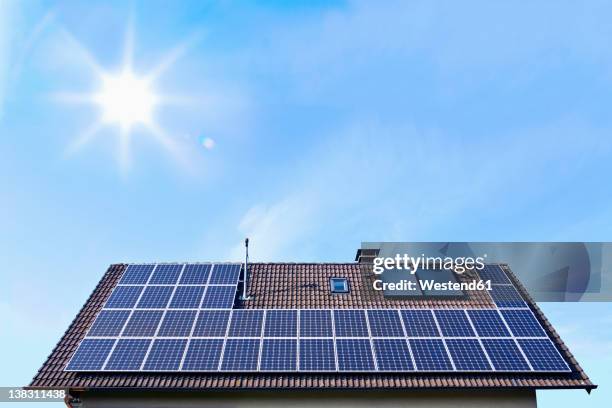 germany, solar panels on houseroof in front of blue sky with sun - zonnepanelen stockfoto's en -beelden