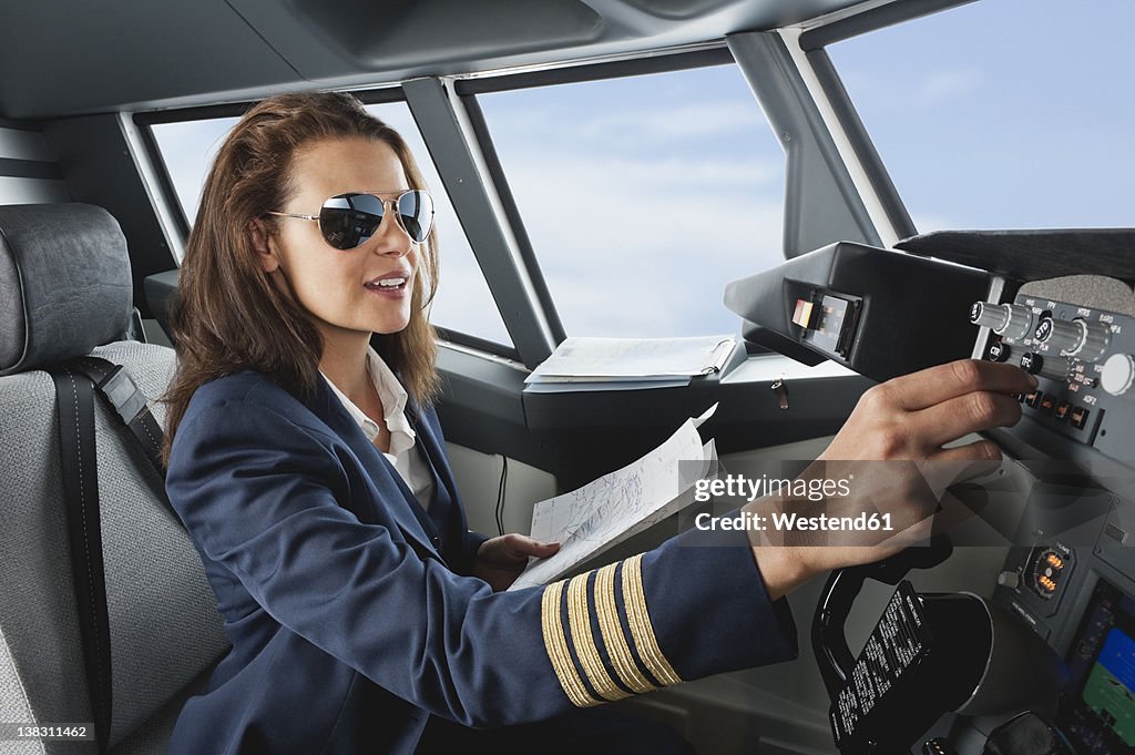 Germany, Bavaria, Munich, Woman flight captain with map in airplane cockpit