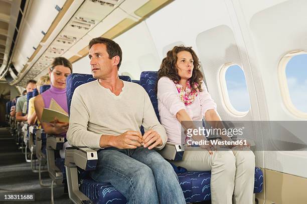 germany, munich, bavaria, passengers reading book in economy class airliner - airplane interior stockfoto's en -beelden