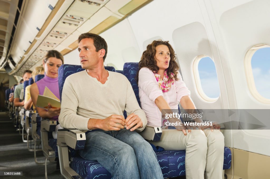 Germany, Munich, Bavaria, Passengers reading book in economy class airliner