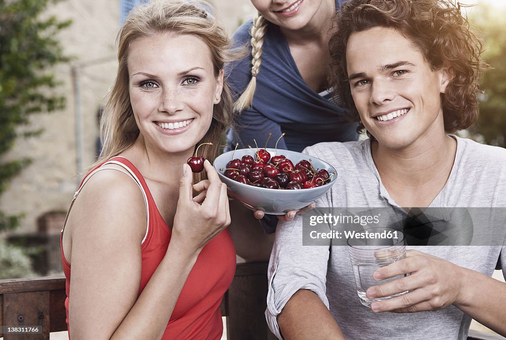 Italy, Tuscany, Magliano, Young man and women with bowl of cherries, smiling