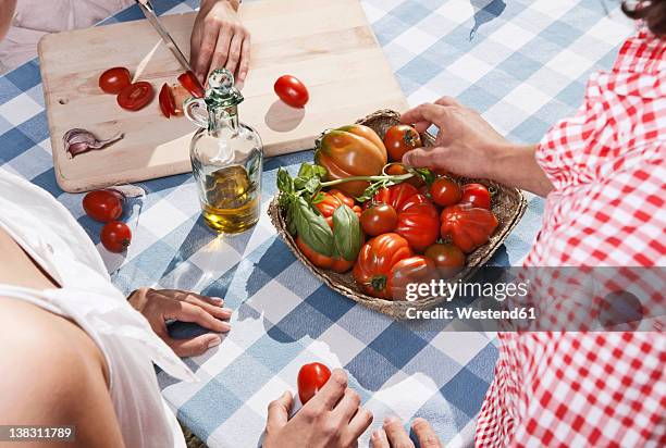 italy, tuscany, magliano, young woman cutting tomatoes on table with friends in foreground - mediterranean diet stockfoto's en -beelden
