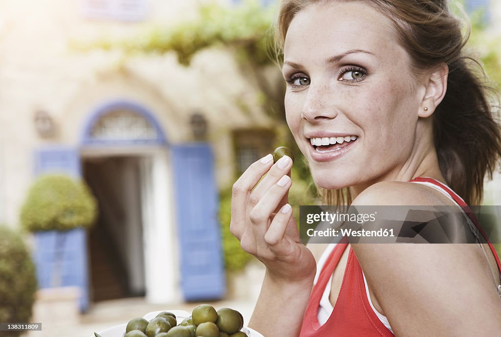 Italy, Tuscany, Magliano, Young woman holding green olives, smiling, portrait