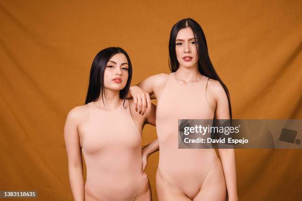 two confident women in beige bodysuit looking serious at camera while posing together on an isolated background. - skin colored body suit stock pictures, royalty-free photos & images