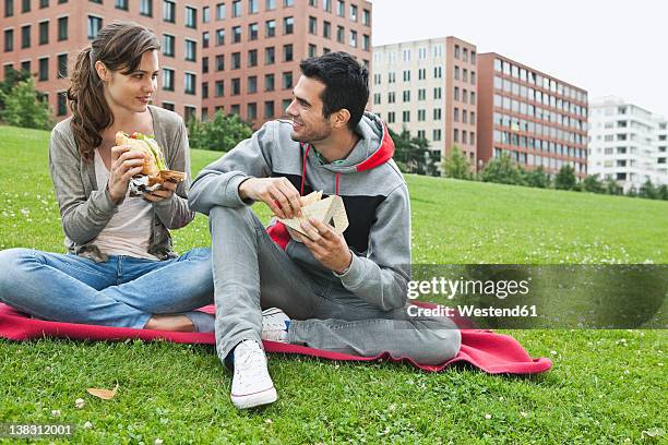 germany, berlin, couple eating food in park - man holding a burger stock pictures, royalty-free photos & images