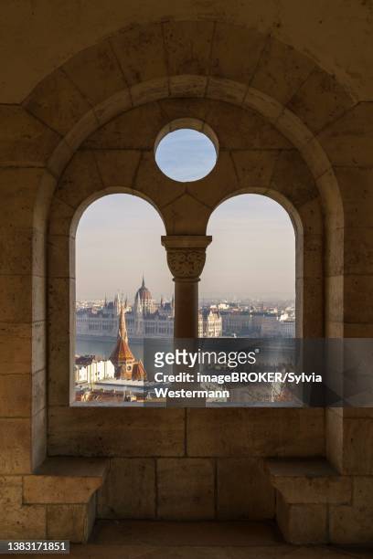 view through an arched window of the fishermen's bastion onto the danube with the parliament building, budapest, hungary - fishermen's bastion stock pictures, royalty-free photos & images