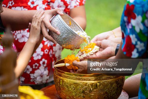 asian little child girl pouring water on hands of elder senior - songkran stock pictures, royalty-free photos & images