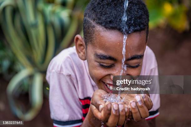 giovane ragazzo africano che beve acqua dolce, africa orientale - acqua potabile foto e immagini stock