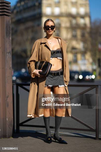 Leonie Hanne wears gold pendant chain necklaces, black sunglasses, black monogram earrings from Miu Miu, a dark gray ripped shoulder-off / cropped...