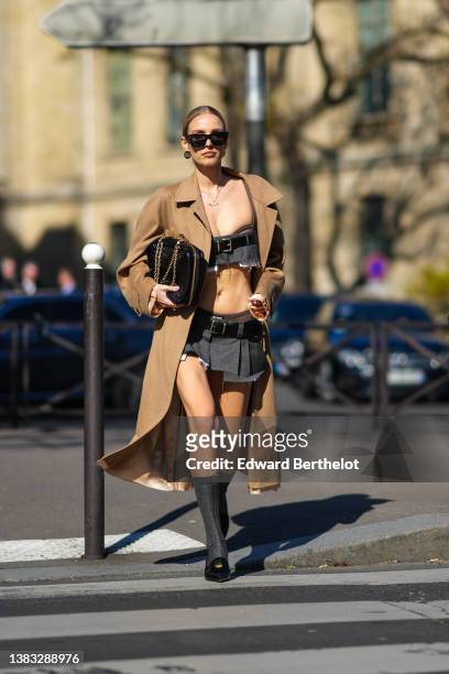 Leonie Hanne wears gold pendant chain necklaces, black sunglasses, black monogram earrings from Miu Miu, a dark gray ripped shoulder-off / cropped...