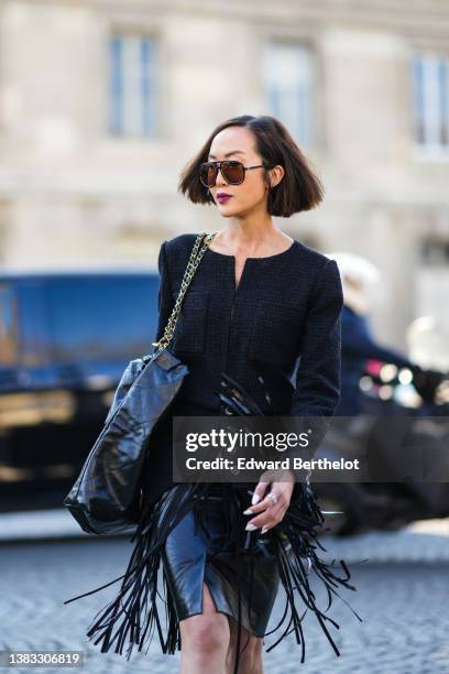 Chriselle Lim wears sunglasses, a black tweed buttoned jacket from Chanel, large silver chain rings, a black shiny leather shoulder bag from Chanel,...