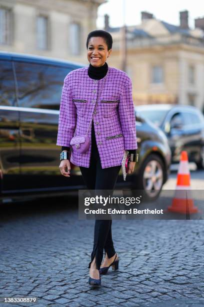 Tamu McPherson wears a black turtleneck pullover, a purple with black checkered print pattern tweed jacket from Chanel, a purple shiny leather...