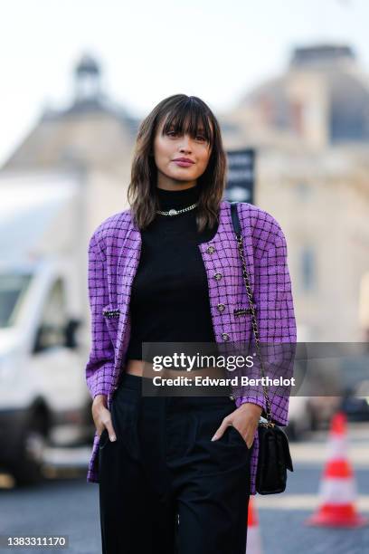 Sarah Ellen wears a silver large chain necklace from Chanel, a black ribbed turtleneck cropped pullover, a purple with black checkered print pattern...