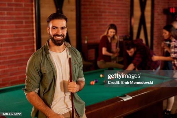 retrato de um homem novo com seus amigos que jogam o jogo da associação no fundo - snooker - fotografias e filmes do acervo