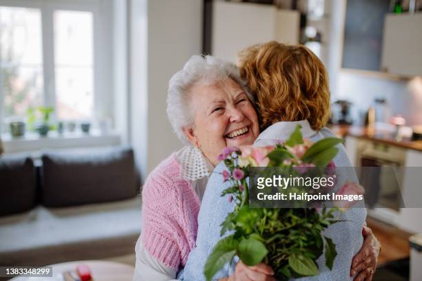 happy senior mother getting flowers from her adult daughter at home, mother's day concept. - mother congratulating stock pictures, royalty-free photos & images