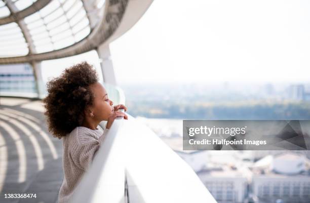 little multiracial girl with afro hairstyle standing on bridge and looking at city view outdoors. - girl side view stock-fotos und bilder