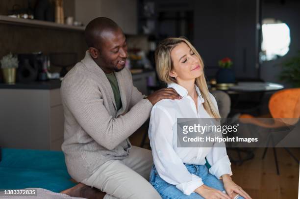 mid adult biracial couple in love sitting and resting together at home. - girlfriend massage ストックフォトと画像