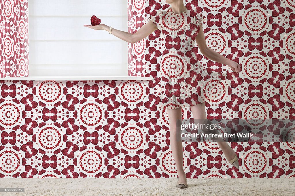 Woman holding red heart blends into the wallpaper