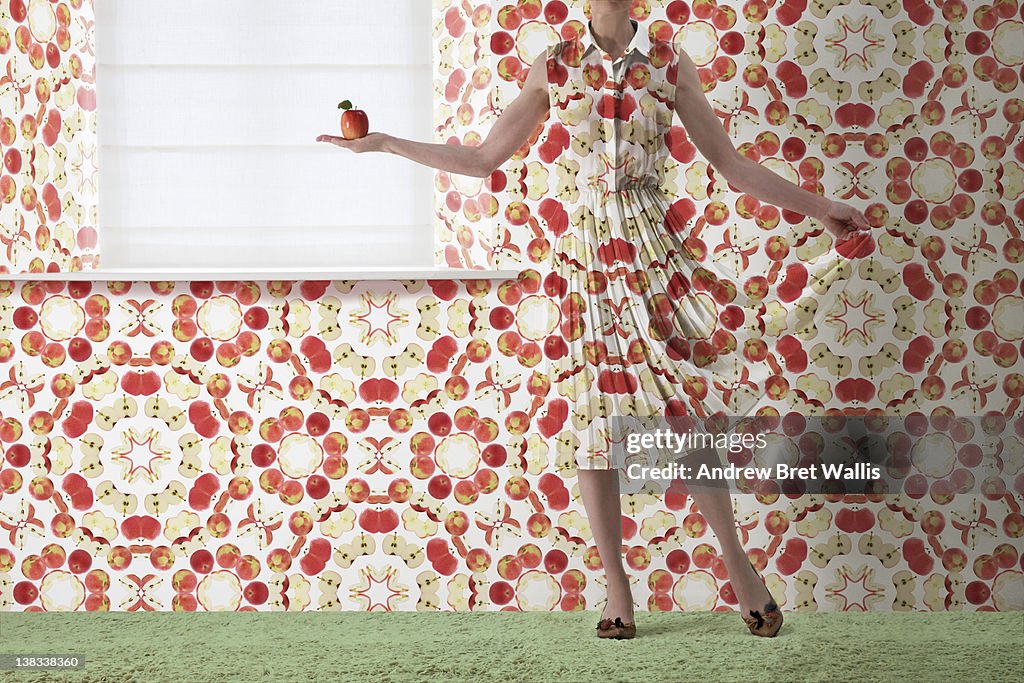 Woman holding red apple blends into the wallpaper