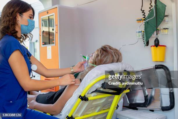 young female paramedic with face mask helping a patient with respirator in ambulance during pandemic - respiratory tract stock pictures, royalty-free photos & images