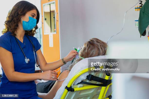 junge sanitäterin mit gesichtsmaske hilft einer patientin mit atemschutzgerät im krankenwagen während einer pandemie - fake hospital stock-fotos und bilder