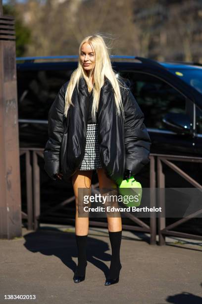Thora Valdimars wears a black V-neck t-shirt, a black oversized puffer jacket, a black and white houndstooth print pattern short skirt, a neon green...