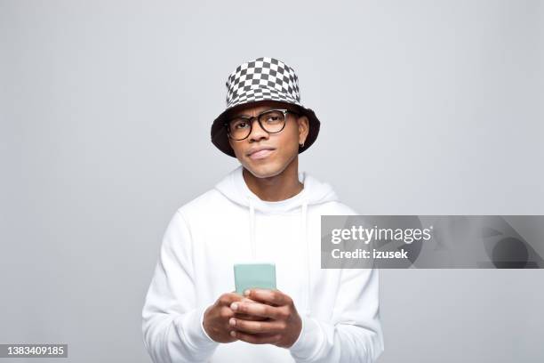 portrait of confused young man using smart phone - bucket hat stock pictures, royalty-free photos & images