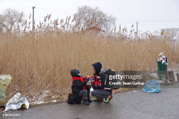 Tatiana Kostyuk helps her son Jan eat a sausage from a nearby aid station upon their arrival from war-torn Ukraine at the Medyka border crossing on...