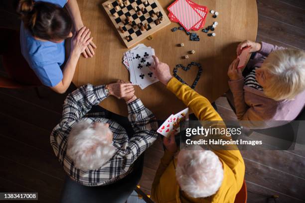 top view of seniors playing a board game in their retirement home, nurse is playing with them. - assisted living community stock pictures, royalty-free photos & images