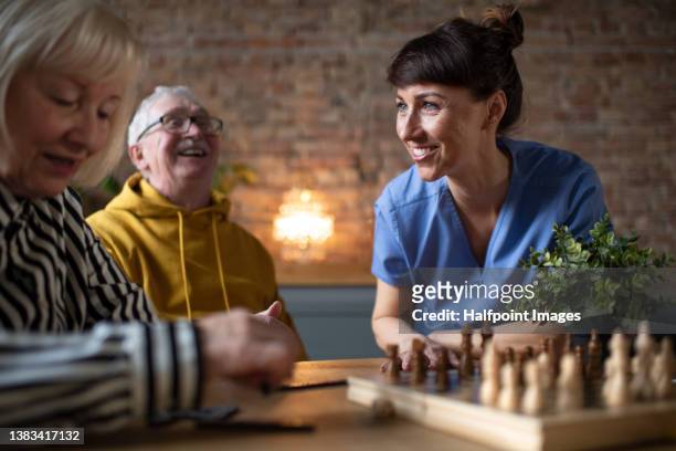 seniors playing a board game in their retirement home, nurse is playing with them. - assisted living community stock pictures, royalty-free photos & images