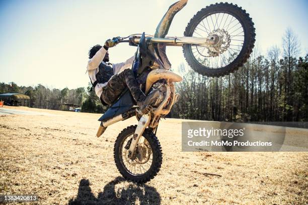 dirtbiker doing a wheelie through a field - wheelie stock pictures, royalty-free photos & images